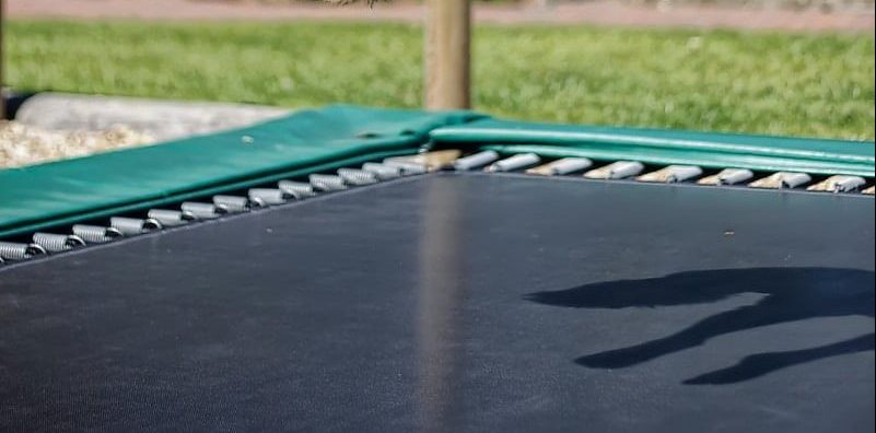 What Is the Best Rectangle Trampoline on the Market? man in white t-shirt and blue and white plaid shorts sitting on blue metal bench